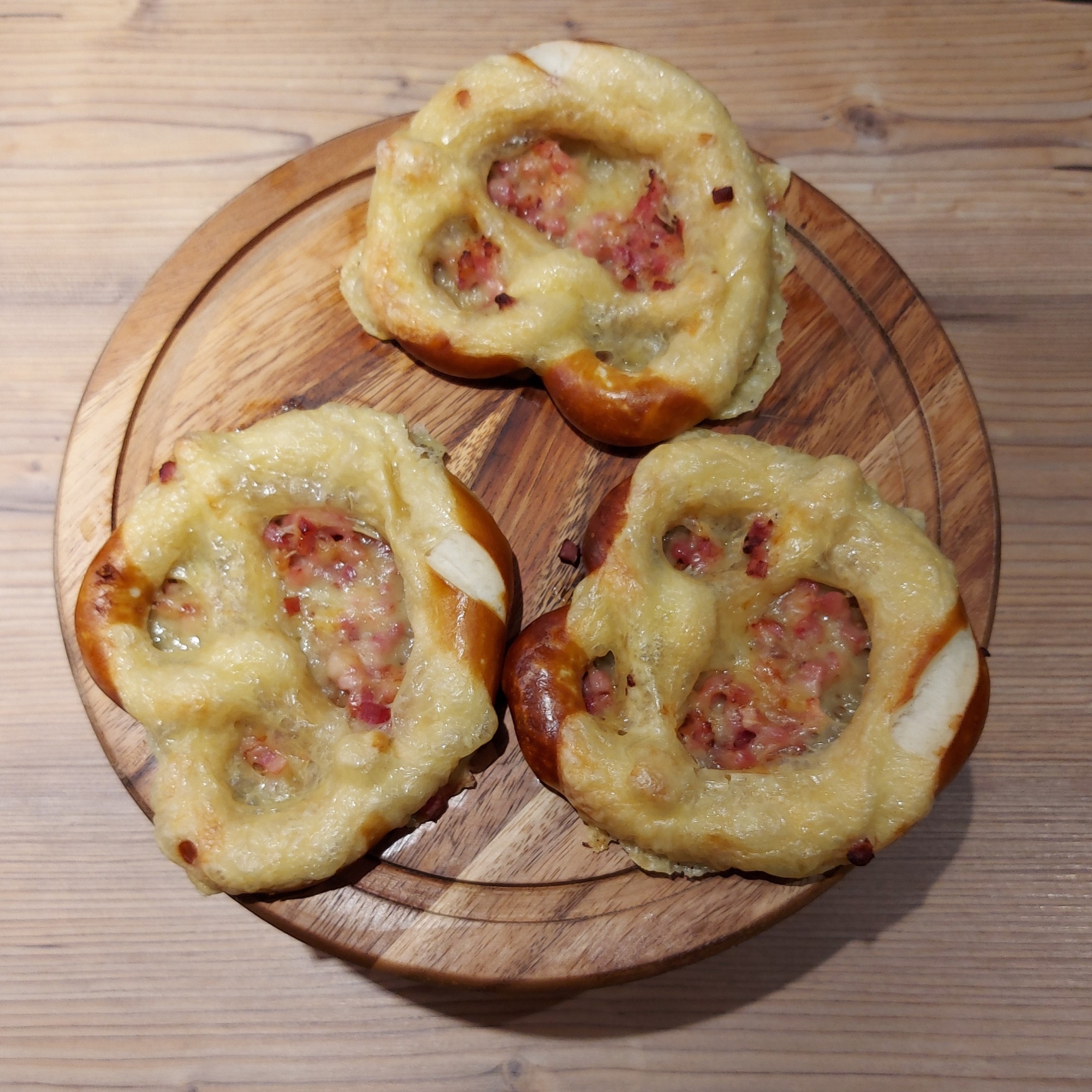 Drei Brezen mit Speck und Käse überbacken, angerichtet auf einem Schneidebrett aus Holz auf der Theke der Brotzeithütte am Autohof.