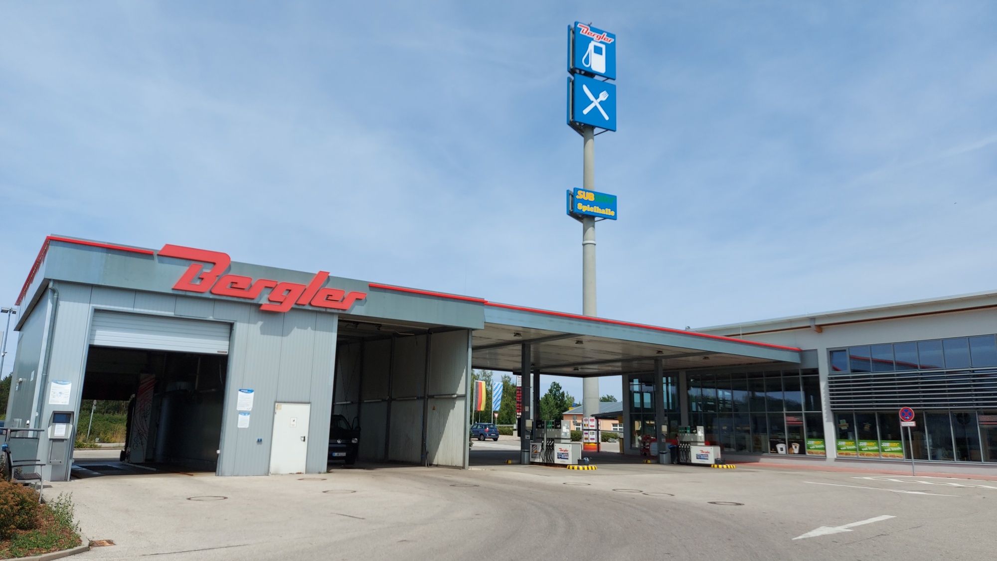Links Waschanlage und SB-Waschbox, auf dem Dach das rote Bergler Logo. Rechts angrenzend der Tankplatz und das Gebäude des Autohofes.