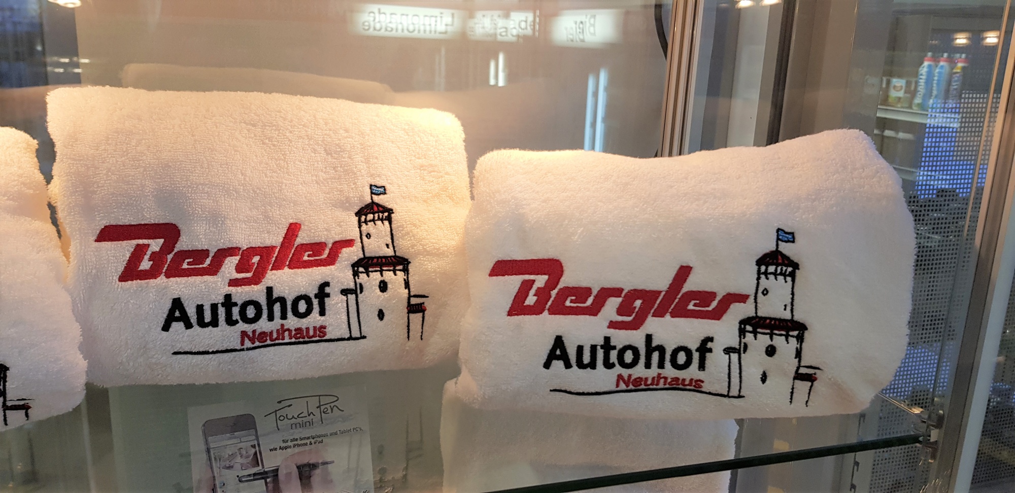 weiße Saunatücher in der Vitrine mit dem Logo des Bergler Autohofs bestickt.